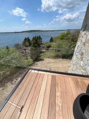 Frameless glass railing at the corner of a hardwood deck beside a stone wall overlooking a bay.