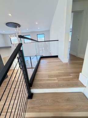 Black cable stair railing transitions to frameless glass in a base rail along a white oak upper landing.