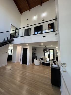 Dark floating treads rise to a balcony edged with frameless glass on a black base rail in a vaulted room.