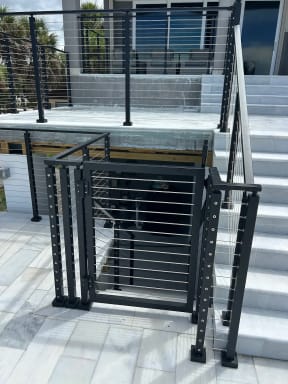 A black cable railing gate and posts sit at the base of white marble exterior steps.