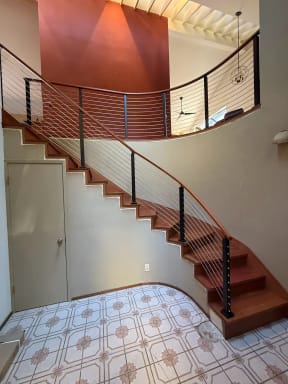 Black posts and a curved wood handrail with stainless cables follow a sweeping curved stair to a curved balcony.