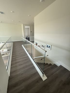 Frameless glass in a white base shoe with a slim cap and a glass-mounted handrail follows a dark-plank stair down from an upper hall.