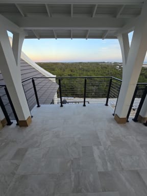 White timber braces frame a tiled covered balcony with black cable railing looking out over forest.