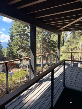 Black posts with wood cap and cable infill guard a covered deck overlooking pines and mountains.