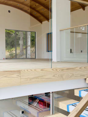 Frameless glass mounted to the face of a wood fascia lines a loft beneath a curved wood ceiling
