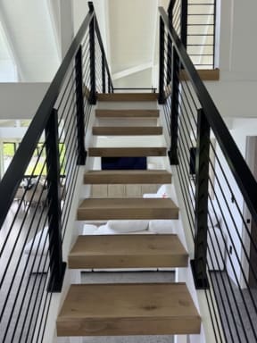 View up an open-riser oak stair flanked on both sides by black horizontal rod railing.