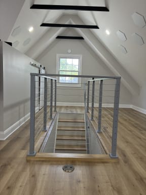 Silver cable railing guards a stair opening in a bright attic bonus room with wood floors.