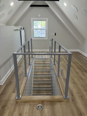 Symmetric view of a stair opening framed by silver cable railing in a vaulted attic room.