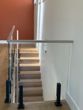 Glass panels on black talons with a white oak cap guard a stair opening beside a terracotta accent wall.
