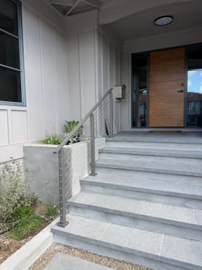Gray stone front entry steps with a gray aluminum cable railing leading to a wood front door.
