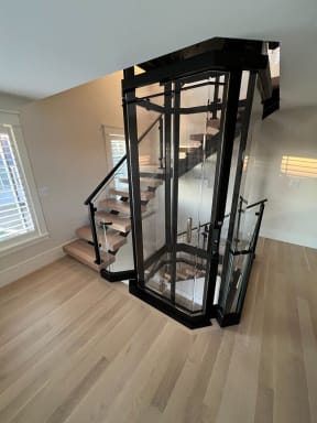 Oak floating treads on a black mono stringer with post-to-post glass wrap around a glass residential elevator.