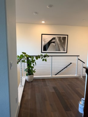White-post cable railing with black top rail encloses a stair opening on dark wood flooring.