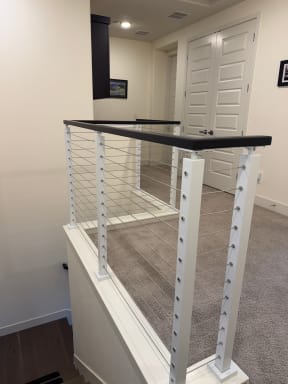 Bright white cable posts and black cap rail guard a carpeted stair opening in a hallway.