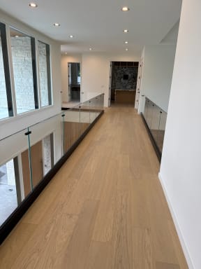 Frameless glass railing in a dark base rail lines both sides of a white oak bridge hallway.