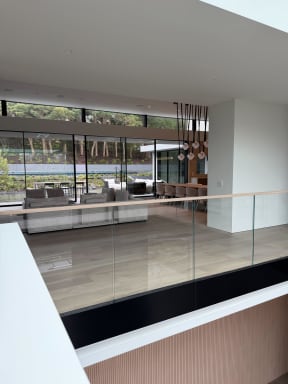 Frameless glass railing with wood cap edges an upper floor overlooking a living space and wall of windows.