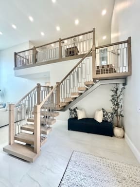 A floating mono stair with oak treads, wood newels and geometric metal balusters climbs to an open loft in a bright foyer.