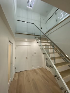 Glass panels on standoff pins with a wood handrail follow an open-riser oak stair up to a glass balcony.