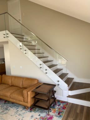Glass panels on stainless standoff pins with a stainless handrail climb a stair above a leather sofa.