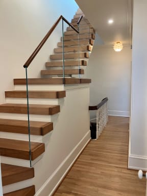 Thick wood treads with a frameless glass panel and wood handrail retrofitted onto a stair in a white hallway.
