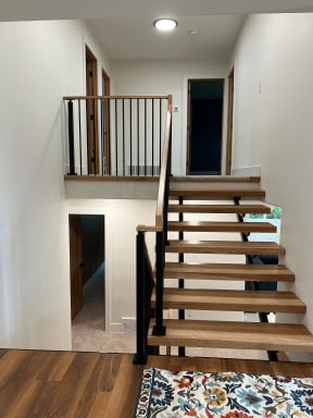 Hickory open treads on black stringers with black balusters and handrail rising to a balcony landing.