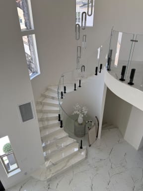 Curved frameless glass railing on black Ascend Talons follows a white marble curved staircase and balcony.