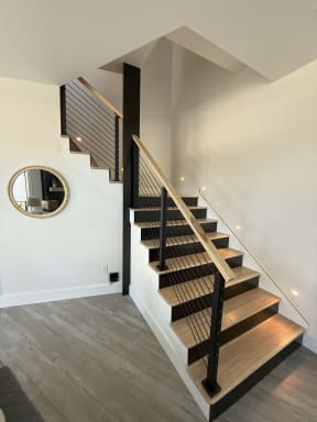 Black posts with horizontal rods and a light oak handrail follow a switchback stair with oak treads and black risers.