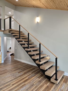 Thick oak floating treads on a black stringer rise to a loft with black-post cable railing and a light wood handrail.