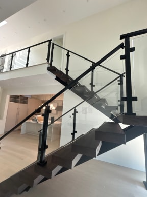 Extra-wide dark wood floating treads on black stringers with black-post glass railing in a bright modern home.