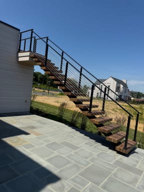 Hardwood floating treads on a black mono stringer climb a white home's exterior to an upper deck, edged by black cable railing.