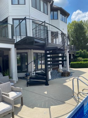 Black spiral stair with cable railing connects a pool patio to a balcony with matching cable railing.