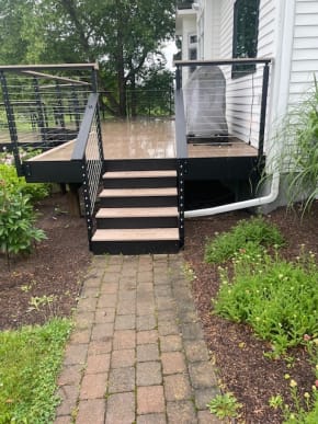 Black side-mount cable railing and beverage rail wrap a composite deck and short stair above a brick path.