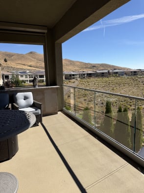 Frameless glass with a metal top cap encloses a covered concrete patio overlooking desert hills.