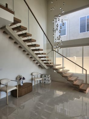 Oak floating stair with white stringer and frameless glass with wood handrail rising beside a crystal chandelier over polished marble.