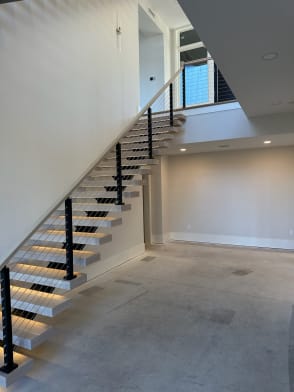 White oak floating treads with LED lighting on a mono stringer with black cable railing rising to a loft.