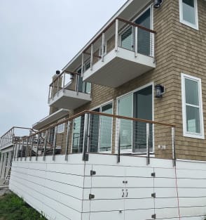 Stainless side-mount posts with rod infill and wood caps on stacked balconies of a shingled coastal home.