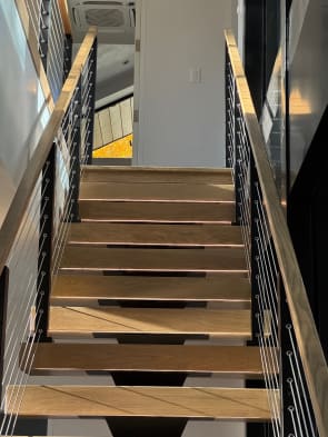Wood treads on a black mono stringer climb between cable railings with wood handrails toward a bright landing.
