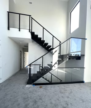 Black floating switchback stair with cable railing and base rail glass in a white stairwell