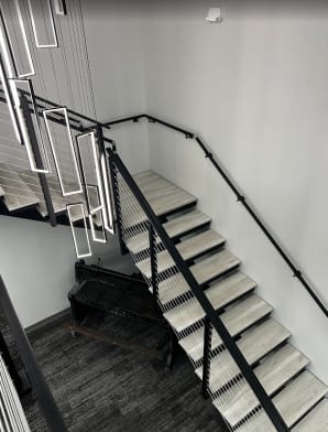 Light gray treads on a black steel stair with cable railing and wall handrail beneath hanging LED pendants.