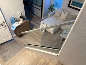 Frameless glass in a silver base rail with an aluminum cap guards a stair opening beside a living room