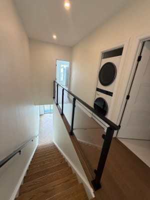 Black posts and glass panels with a black cap guard a stair opening in a white hallway.