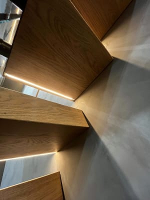 White oak cantilever treads with recessed LED strips throw dramatic light patterns on a smooth plaster wall.