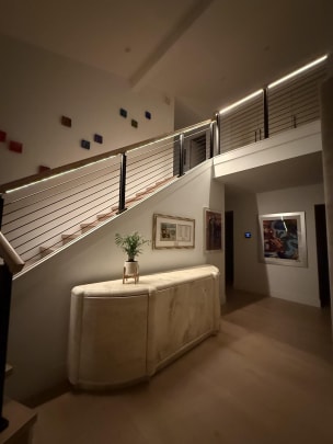 Black cable railing with a wood handrail glowing with integrated LED light runs up a stair and along a balcony.