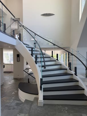 Sweeping white curved stair with dark treads lined by glass railing on black talon clamps and a curved handrail.