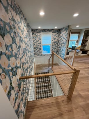 Oak newels and handrail with stainless cable infill wrap a stair opening against bold floral wallpaper.