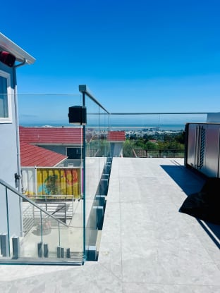 Frameless glass on stainless talons runs along a pale stone rooftop terrace overlooking the city and bay.