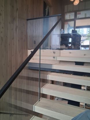 Glass railing with black handrail over floating treads