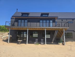 Black cable railing spans a long elevated deck on a dark modern farmhouse