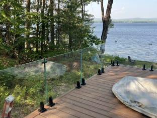 Frameless laminated glass on jet black surface talons edges a deck among pines above a lake