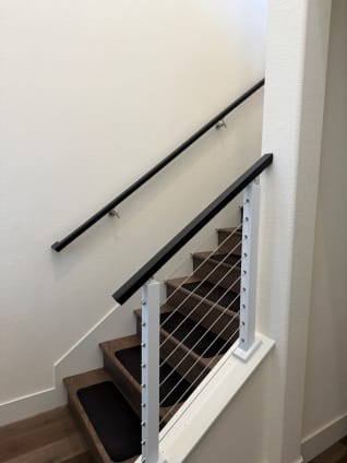Bright white cable posts with a black top rail and matching wall handrail along an interior stair.