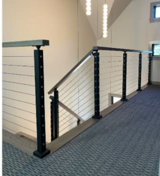 Black posts with stainless cable infill and a wood cap rail around a carpeted stair landing.